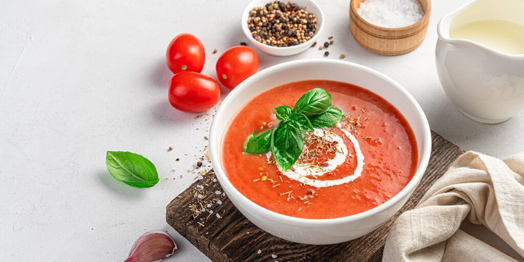 Gri bir arka planda fesleğen ve krema ile domates çorbası.