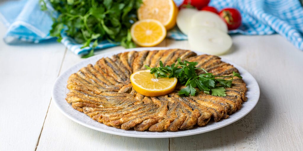 Beyaz ahşap masada beyaz tabakta kızarmış hamsi. Soğan halkaları, domates, maydonoz