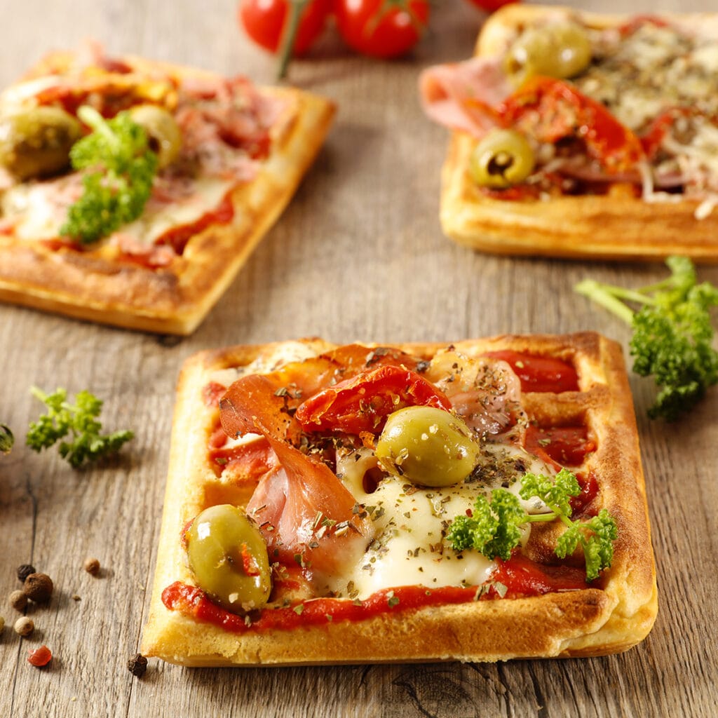 Masanın üzerinde kurutulmuş domates, yeşil zeytin eşliğinde hazırlanmış pizza waffle