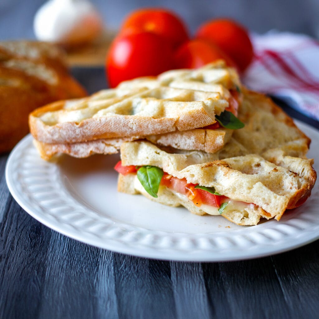 Masanın üzerinde domates, tabağın içerisinde waffle makinesinde hazırlanmış domatesli tost