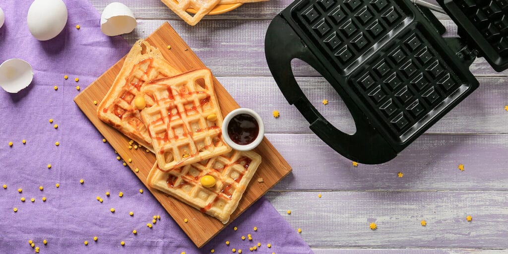 Waffle makinesi, reçel ve yumurta kabukları olan görsel.