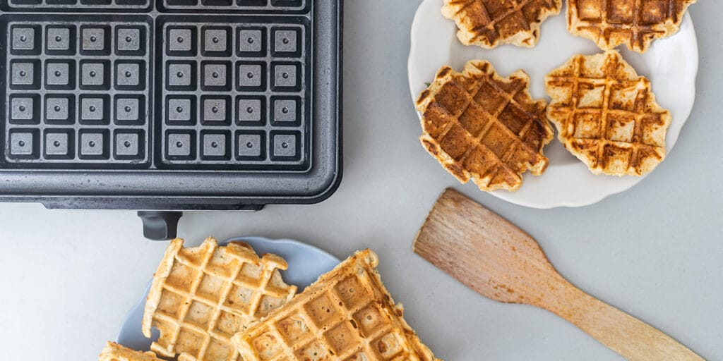 masanın üzerinde waffle makinesi ve yanında lezzetli waffle parçaları olan görsel